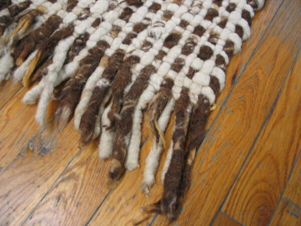 A chunky brown and cream woven rug with thick fringe rests on a warm plank wood floor.