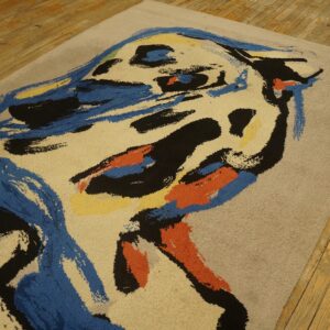 Tan medium-pile rug featuring bold abstract strokes of blue, black, orange, and yellow on wood flooring.