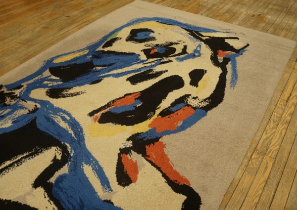 Tan medium-pile rug featuring bold abstract strokes of blue, black, orange, and yellow on wood flooring.