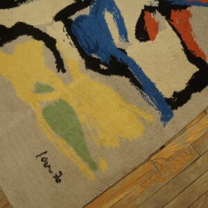 High-pile rug with tan field and colorful abstract shapes of yellow, blue, orange, and black, resting on distressed wood floor.