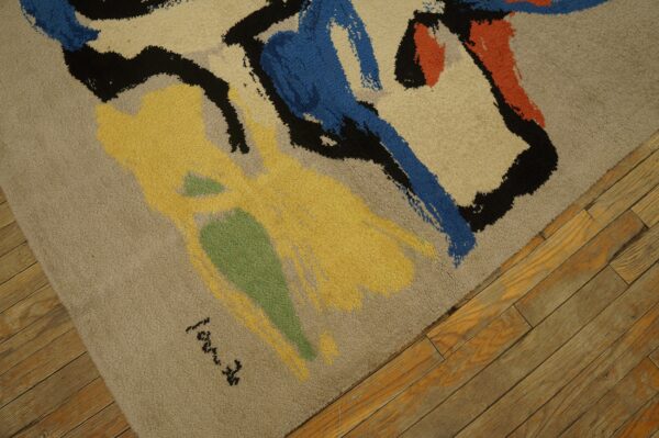 High-pile rug with tan field and colorful abstract shapes of yellow, blue, orange, and black, resting on distressed wood floor.