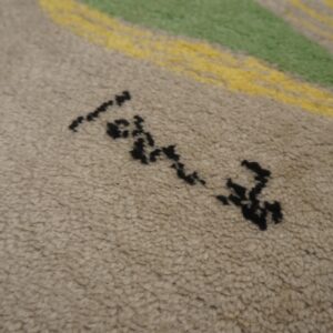 Detail view of a textured beige rug showing black abstract marks and bold green and yellow stripes.