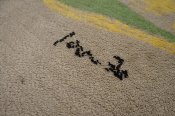 Detail view of a textured beige rug showing black abstract marks and bold green and yellow stripes.