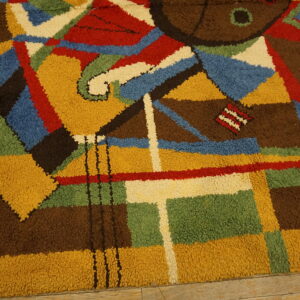 Textured, high-pile rug with a vibrant abstract pattern in brown, yellow, blue, red, green, and cream on wood flooring.