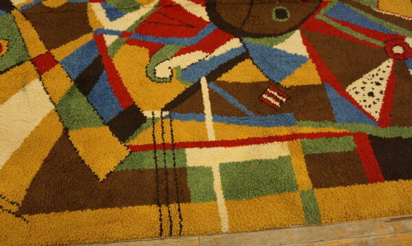 Textured, high-pile rug with a vibrant abstract pattern in brown, yellow, blue, red, green, and cream on wood flooring.