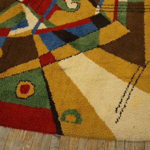 High-pile rug with geometric shapes in primary colors and brown rests on weathered wood planks.