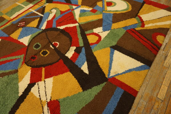 Abstract high-pile rug in brown, yellow, red, blue, and green with a central mask motif on wood floors.