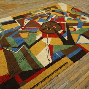 Textured rug with a colorful abstract geometric design in primary colors and earth tones on wood planks.