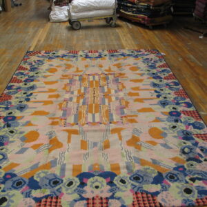 High-pile abstract rug with a central geometric design and a colorful, dense floral border on wood floors.