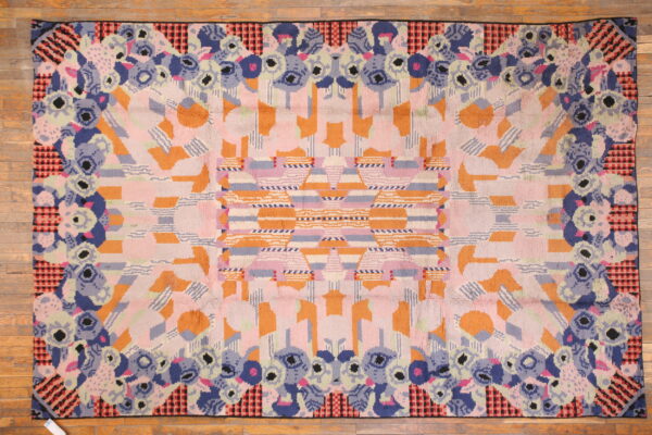 Abstract high-pile rug featuring a border of blue florals and a pink and orange geometric center on wood flooring.