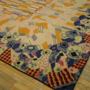 Abstract multicolored rug featuring a dense floral border and a geometric center rests on distressed wood flooring.
