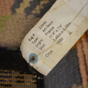 Close-up of a high-pile rug featuring blue, pink, and tan geometric patterns with a descriptive product tag attached.