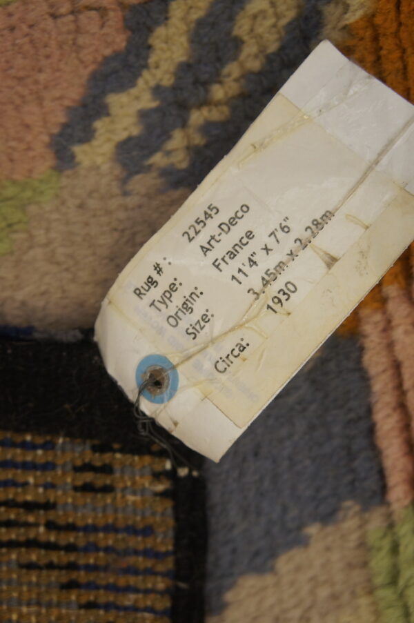 Close-up of a high-pile rug featuring blue, pink, and tan geometric patterns with a descriptive product tag attached.