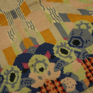 Textured multicolor abstract rug featuring blocks, zigzag lines, and stylized floral motifs on wood flooring.