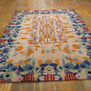 A large, colorful abstract rug featuring geometric and floral patterns in pink, blue, orange, and green on wood flooring.