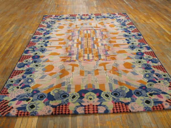 A large, colorful abstract rug featuring geometric and floral patterns in pink, blue, orange, and green on wood flooring.