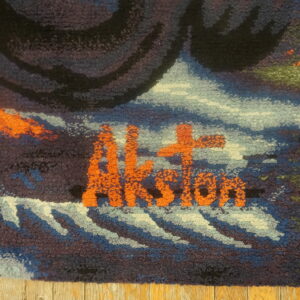 Textured rug detail with orange letters reading "Aksion" surrounded by blue, black, and green loops.