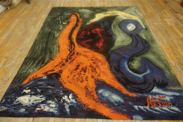 Shaggy abstract rug with bright orange and navy shapes contrasting a dark green background on wood planks.