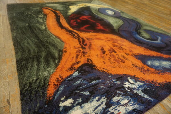 Plush abstract rug featuring bold orange, deep blue, and dark green shapes on light wood flooring.