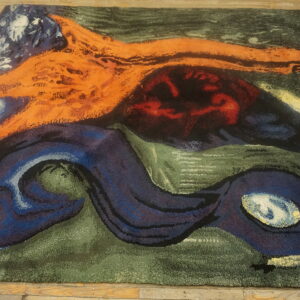 Textured rug with abstract patterns in orange, navy, green, and red lays on wooden planks.