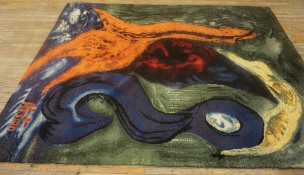 Textured rug with abstract patterns in orange, navy, green, and red lays on wooden planks.