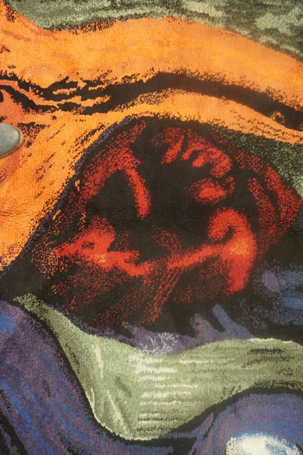 Abstract high-pile rug detailed in vibrant orange, black, red, green, and purple swirling colors.