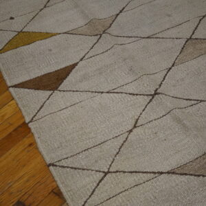 Woven beige rug with abstract brown and mustard yellow geometric lines on wood planks.