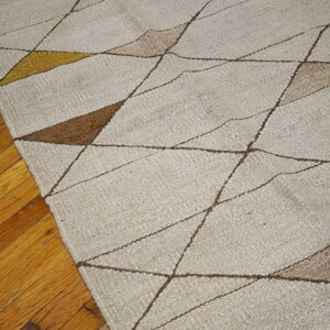 Geometric flatweave rug in beige, brown, and gold rests on a distressed wooden plank floor.