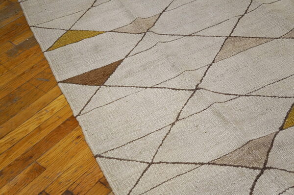 Geometric flatweave rug in beige, brown, and gold rests on a distressed wooden plank floor.