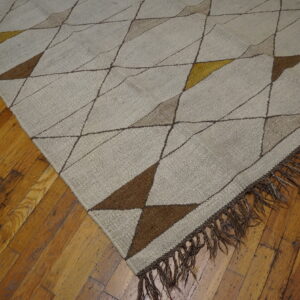 Beige flat-weave rug featuring geometric triangles in brown and gold, laid on worn hardwood flooring.