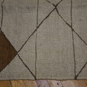Textured beige rug with brown geometric diamond pattern and a solid dark brown triangle resting on wood flooring.
