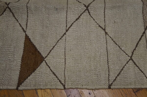 Textured beige rug with brown geometric diamond pattern and a solid dark brown triangle resting on wood flooring.