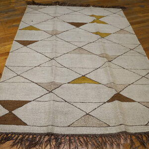 Beige flatweave rug with brown, tan, and gold geometric diamond pattern and fringe on a wood floor.