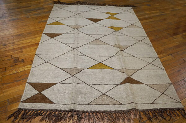 Beige flatweave rug with brown, tan, and gold geometric diamond pattern and fringe on a wood floor.