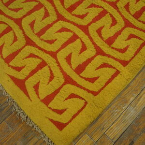 A high-pile rug with a bold yellow and orange geometric pattern sits on rustic wood floors.