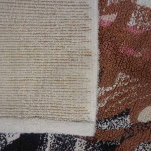 Close-up showing the ribbed woven backing and the thick brown, pink, and white abstract rug pile.