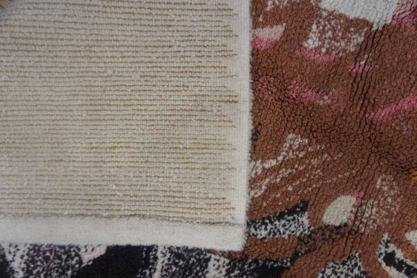 Close-up showing the ribbed woven backing and the thick brown, pink, and white abstract rug pile.