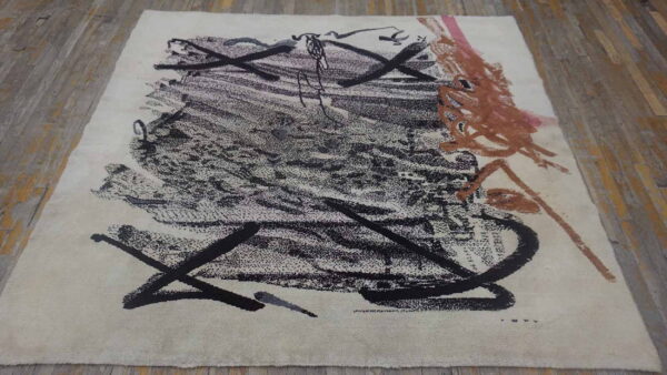 Abstract area rug in cream with sprawling black and terracotta strokes on weathered wood planks.
