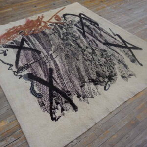 Abstract rug featuring thick black and brown marks on cream pile over gray wood floors.