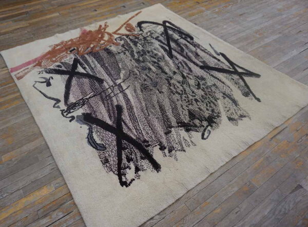 Abstract rug featuring thick black and brown marks on cream pile over gray wood floors.