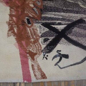 Textured cream rug with abstract black, rust, pink, and gray brushstroke patterns resting on wood flooring.