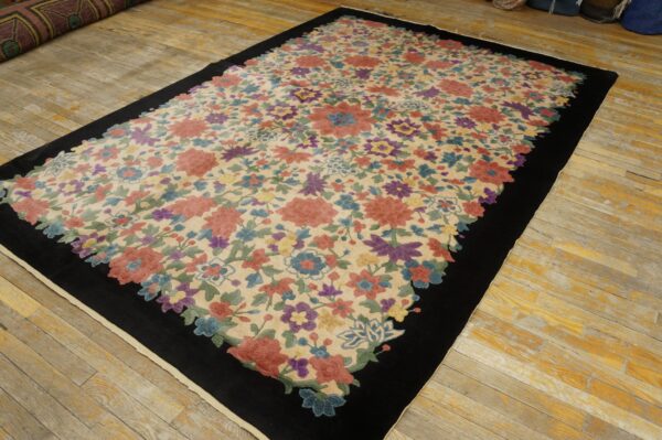 Medium-pile rug featuring multi-colored flowers on cream, framed by a thick black border, placed on plank flooring.