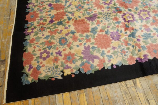 Multicolored floral rug with a beige field and black border rests on distressed wood flooring.