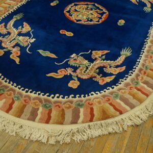 Oval blue rug featuring dragons and a colorful striped border with fringe on rustic wooden flooring.