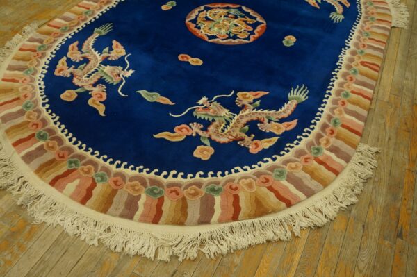 Oval blue rug featuring dragons and a colorful striped border with fringe on rustic wooden flooring.