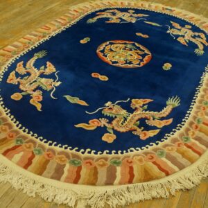 Deep blue oval rug featuring four multicolored dragons, a central medallion, and a wave border on a wood floor.