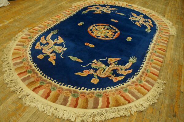 Deep blue oval rug featuring four multicolored dragons, a central medallion, and a wave border on a wood floor.