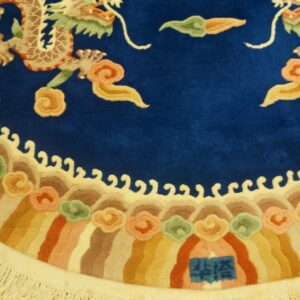 Royal blue rug with detailed light dragons, multicolored striped border, stylized clouds, and light cream fringe.