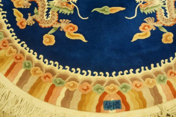 Royal blue rug with detailed light dragons, multicolored striped border, stylized clouds, and light cream fringe.
