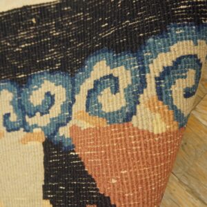 A curled rug edge on wood planks reveals black, blue, terracotta, and cream flatweave patterns.